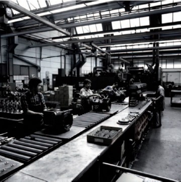 Zwei historische Fotoaufnahmen aus der ehemaligen Produktionshalle, das Arbeiter bei der Montage zeigt. Zu sehen ist das Sheddach, das auch heute den Ausstellungsraum prägt.