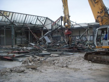 Ein Bagger reißt Teile des Sheddachs sein.